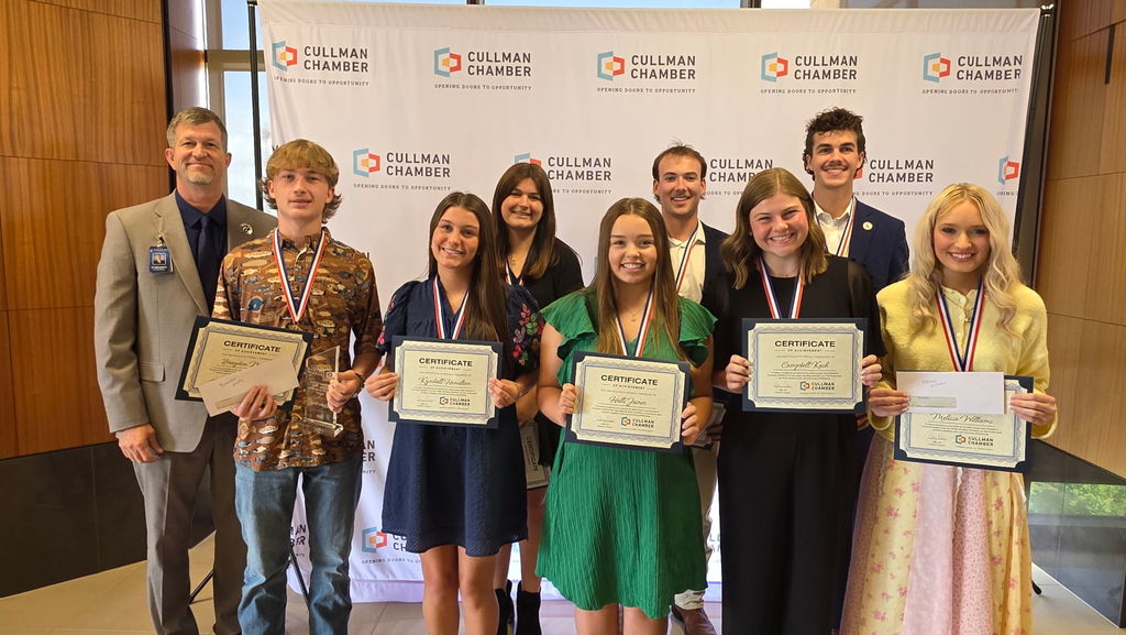 A group of young adults in formal attire holding certificates and smiling for a photo.