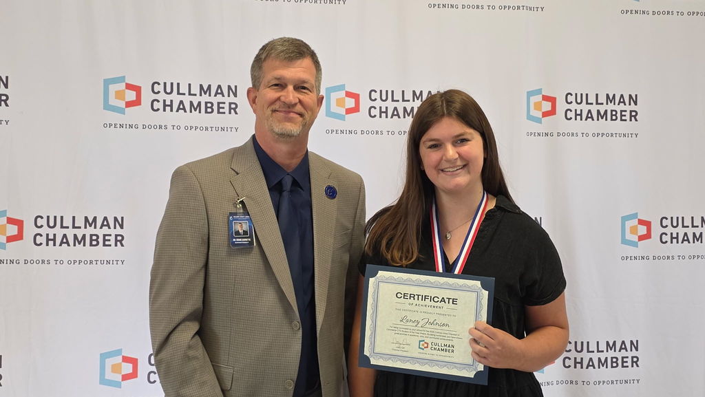 A man and a woman stand with an award plaque; the woman smiles, and the man looks at the camera.