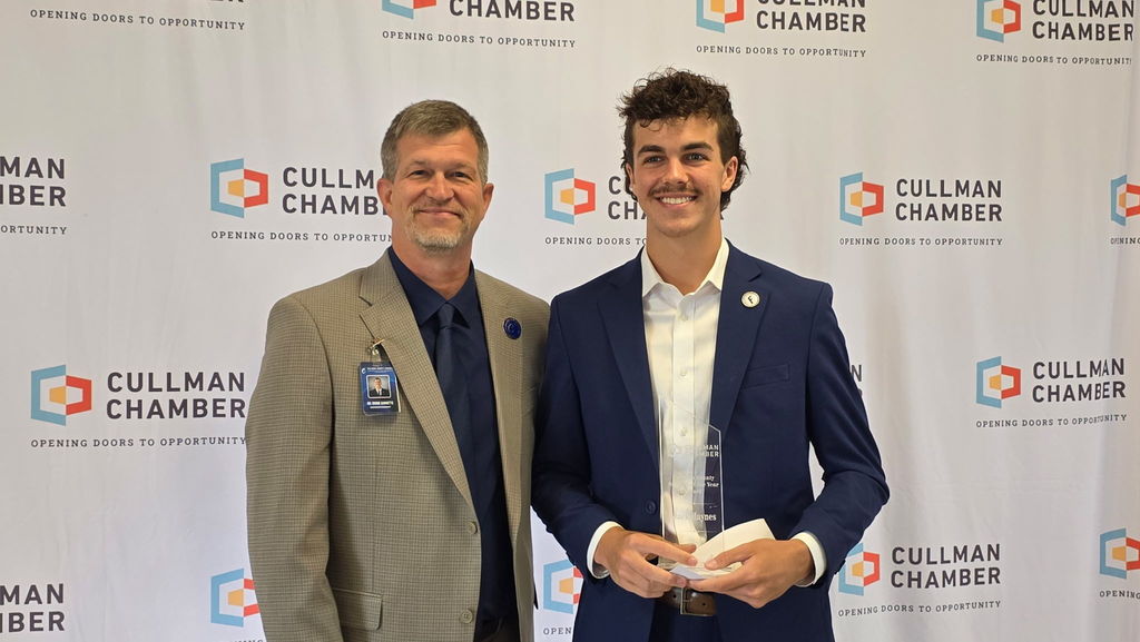 Two men stand before a backdrop with Cullman Chamber branding, smiling, one holding a trophy.