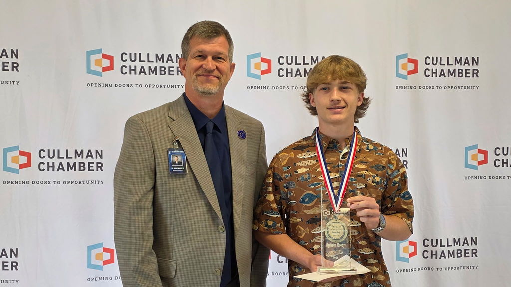 Two men stand before a backdrop with Cullman Chamber branding, smiling, one holding a trophy.