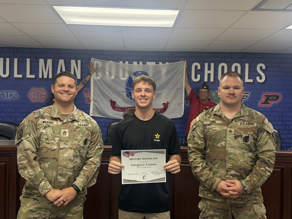 Three men in military uniforms stand next to each other; the middle man holds a certificate.