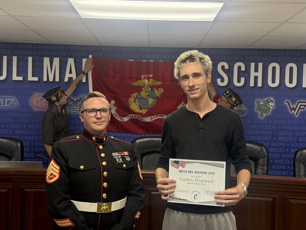 Two men in a conference room. One holds a certificate. The other in a uniform. Behind them, a banner and two men.