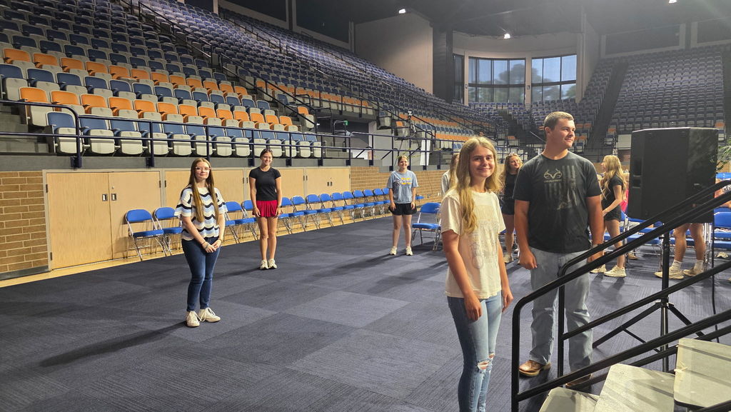 A group of people stand in an auditorium with empty seats and a staircase. Some wear sneakers.