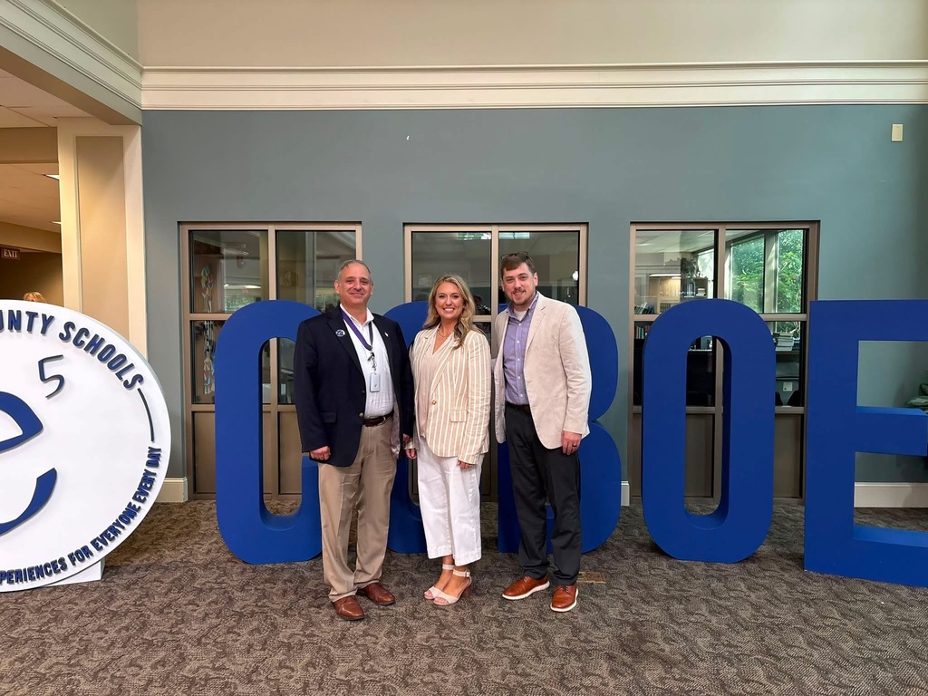 Three people stand behind blue letters spelling "GLOBE" in a room with gray walls. A circular sign with a blue e is on the left.