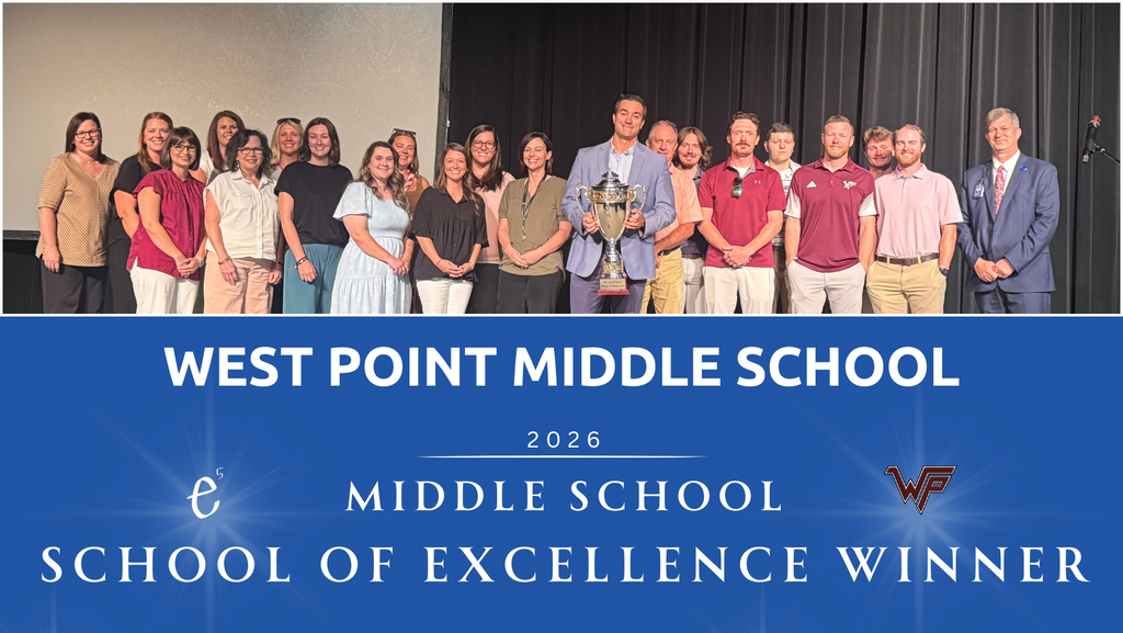 Group of adults and children standing in front of a stage with "West Point Middle School" written above.