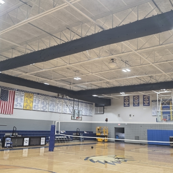 An indoor sports facility with a basketball hoop and a volleyball net, with a high ceiling and metal beams.