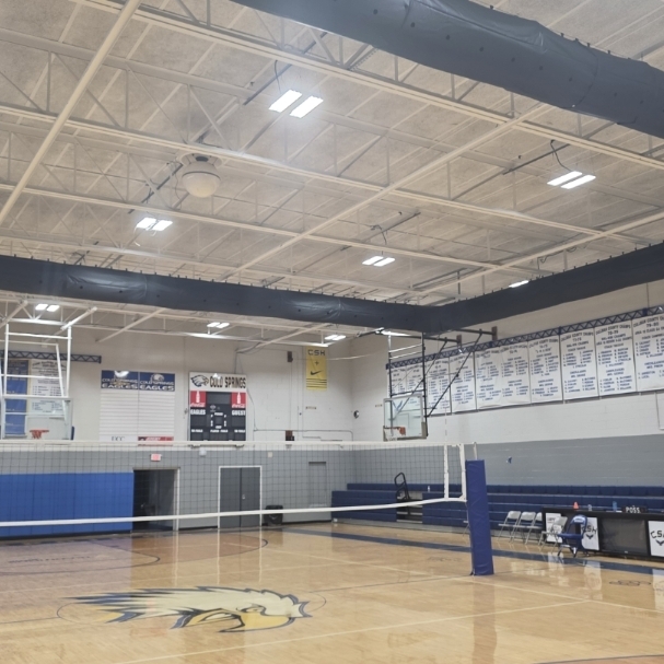 Indoor sports facility with a basketball court, a volleyball net, and a high ceiling with lighting.