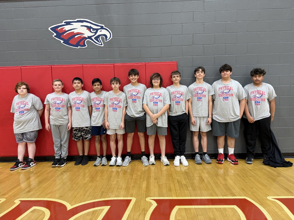A group of students stands on a basketball court in front of a wall with a logo.