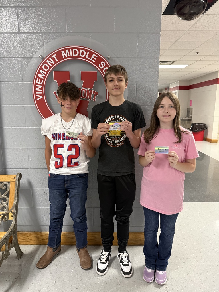 Three students in a school hallway, each holding a certificate, standing before a Vinemont Middle School sign.