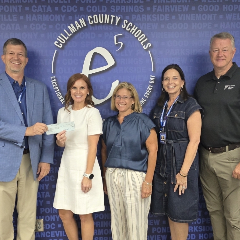 Five people stand in front of a blue backdrop with text. They are holding a check.
