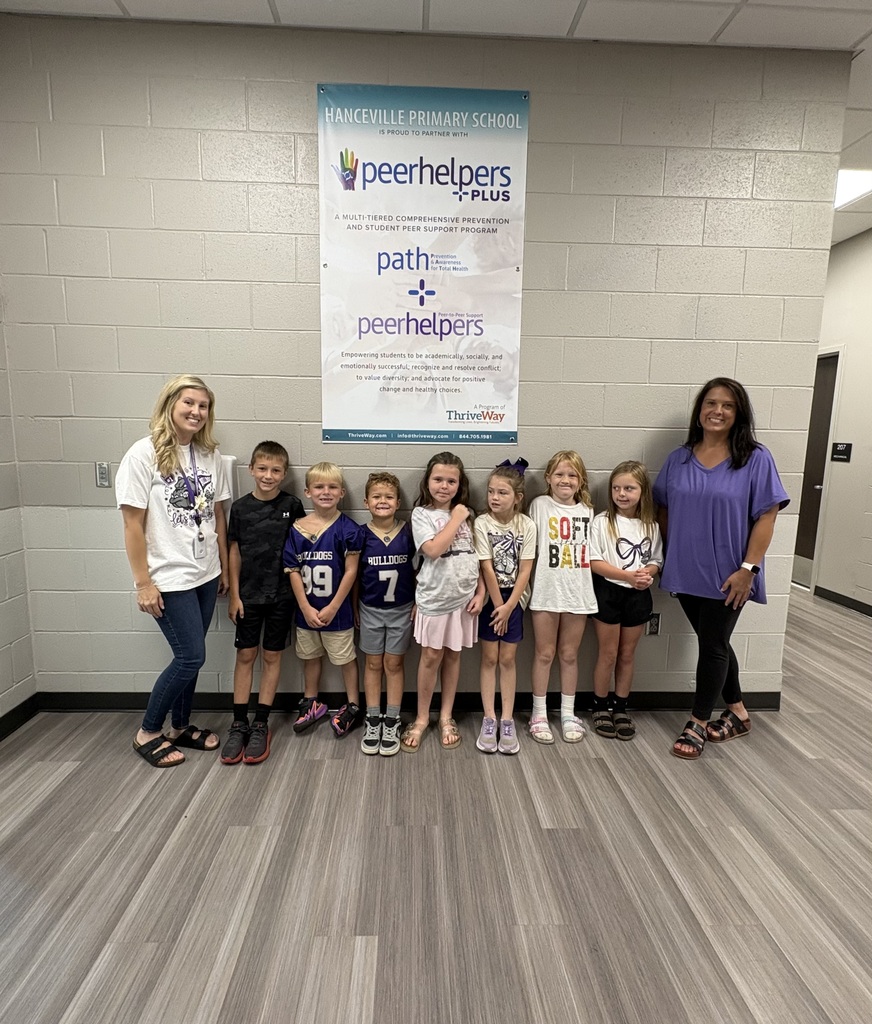 A group of children and adults stand in a room with a banner that reads "Peerhelpers" in the background.