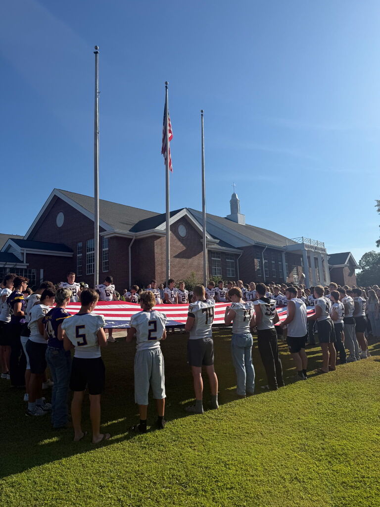 A group of people holds an American flag in a row on a sunny day.