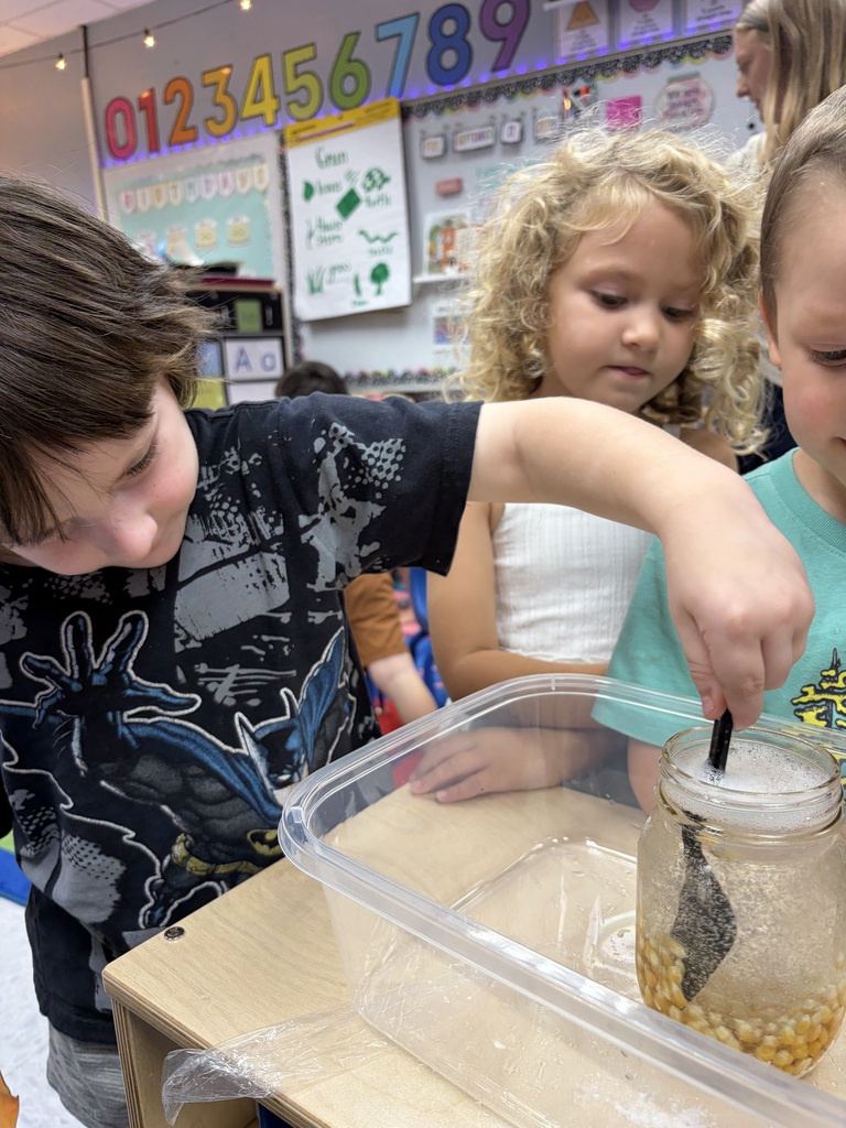 Children work together, one holding a stick over a container while another dips it into liquid.