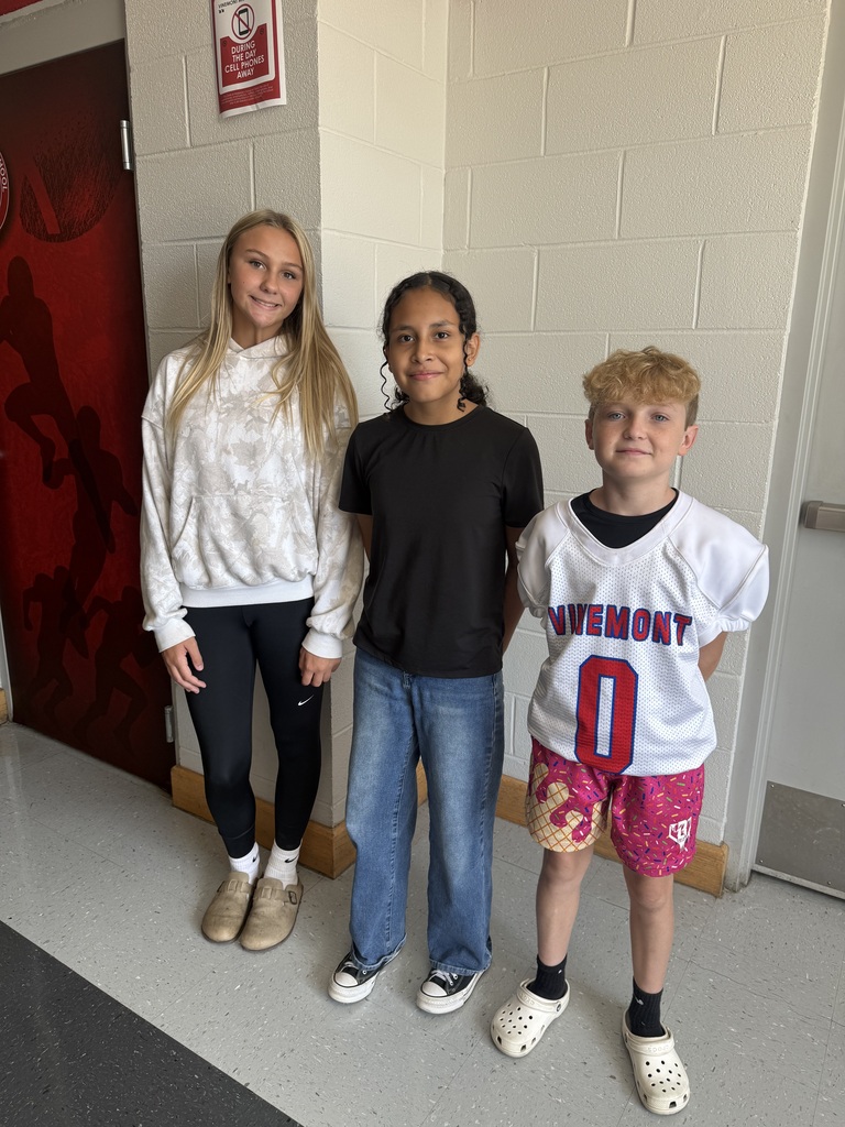 Three children stand next to each other in a hallway. Two doors and a wall are behind them.