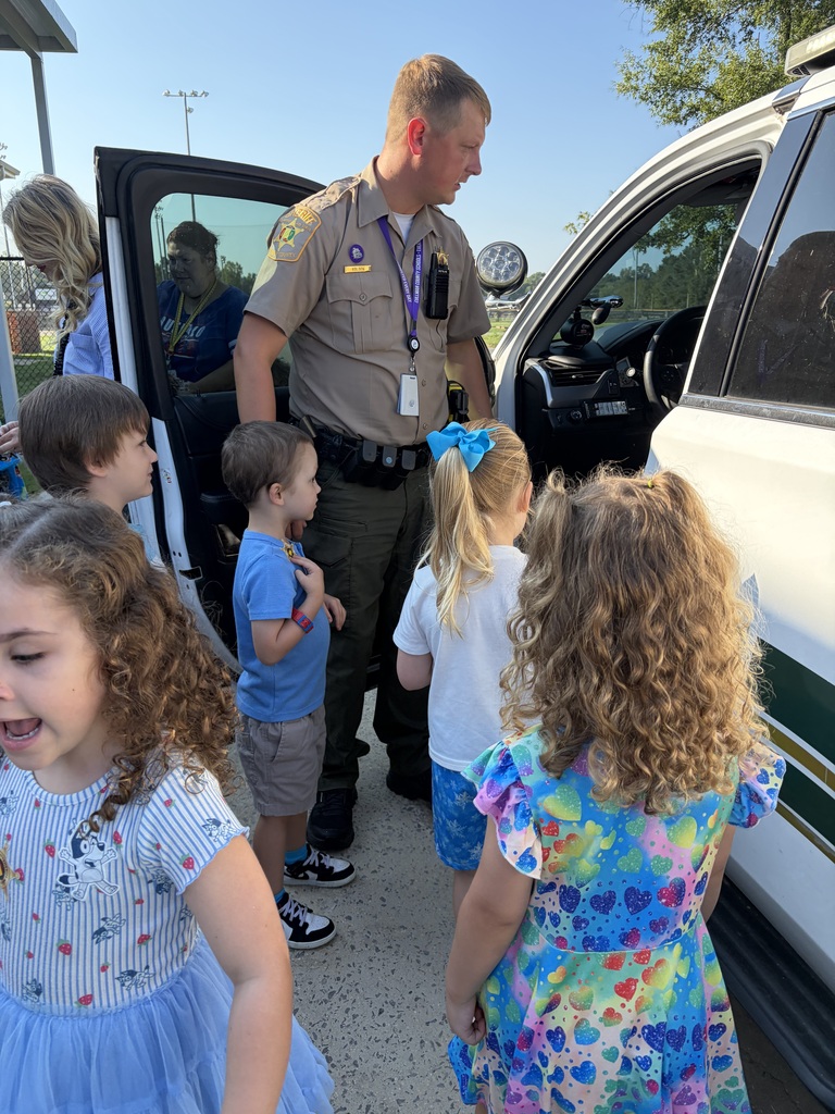 A group of children and a police officer are gathered in front of a vehicle. The officer is talking to them.
