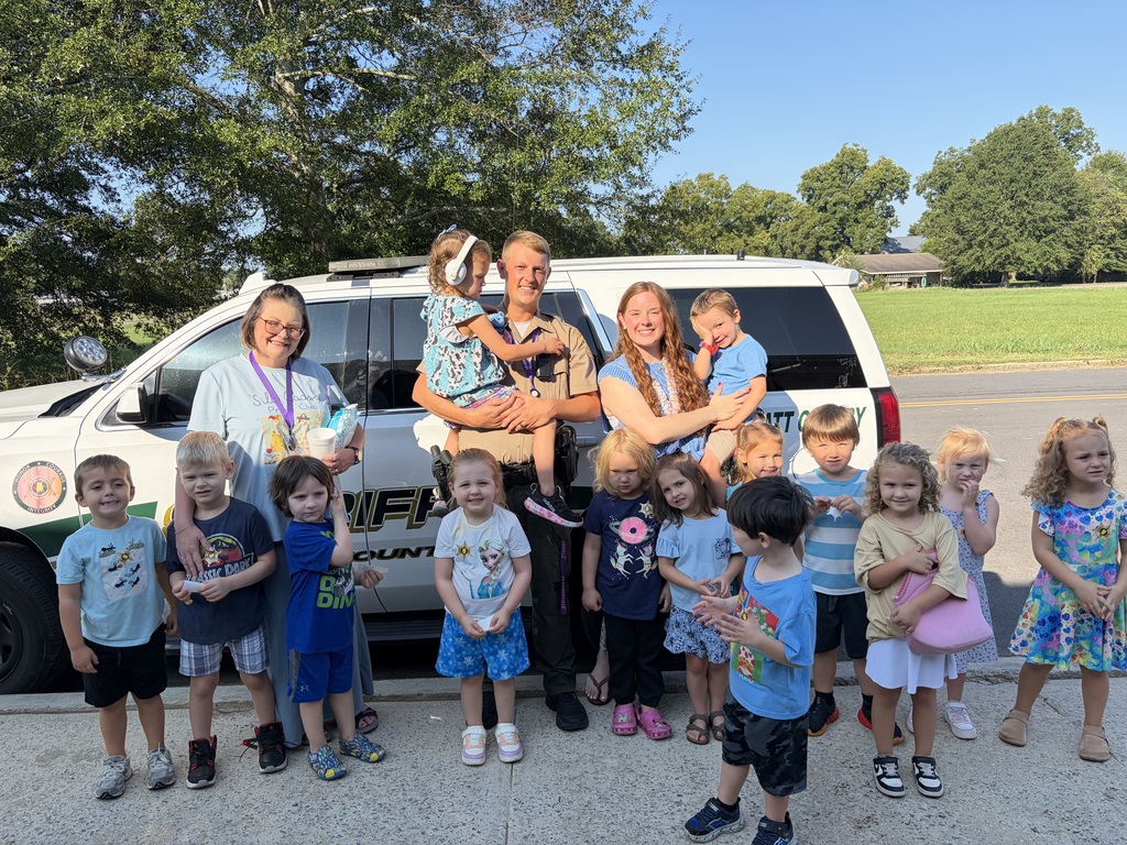 Group of children and adults standing in front of a white SUV with green and white markings.