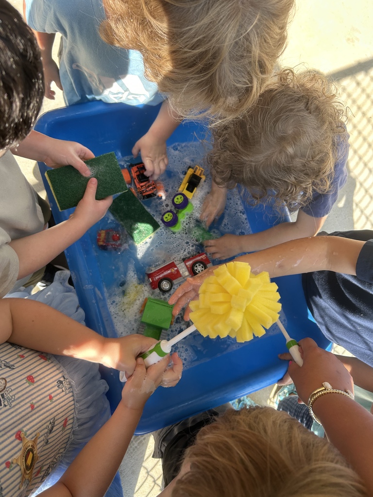 A group of children are playing with water, toys, and brushes in a blue tray.