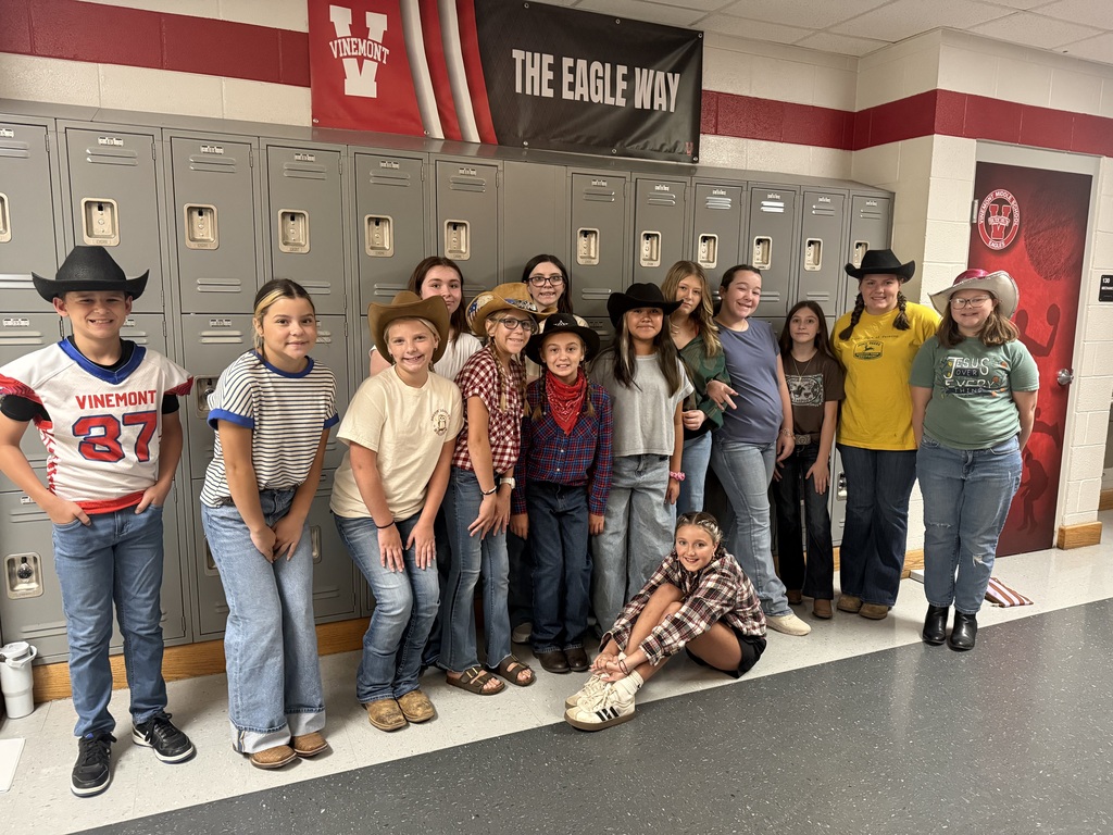 A group of students in a hallway with lockers, some wearing hats, sneakers, and boots, and one sitting.