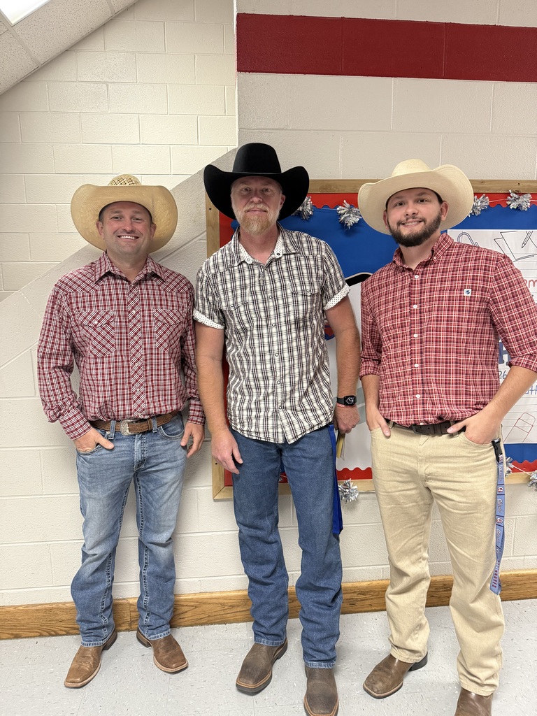Three men in cowboy hats and jeans stand together in a room with a red and white wall.