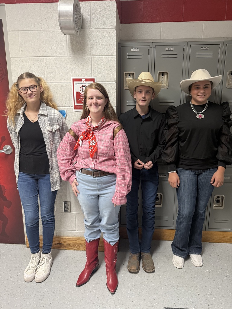 Five young people, some in cowboy hats, stand in a hallway, smiling and posing for a picture.