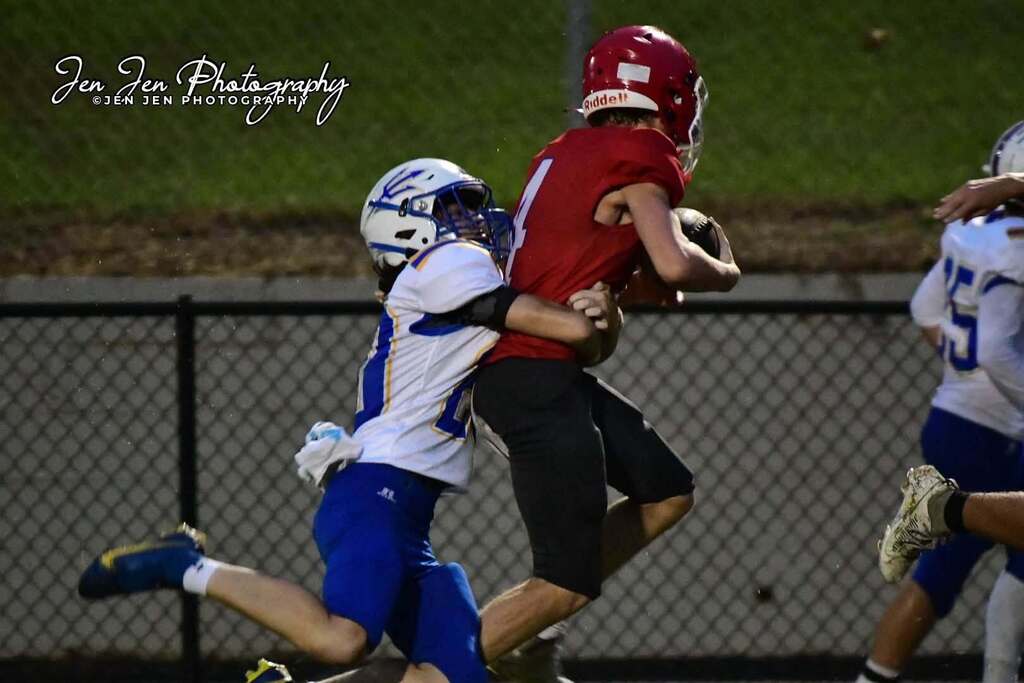 Two football players in action on the field; one in red tackles another in blue.