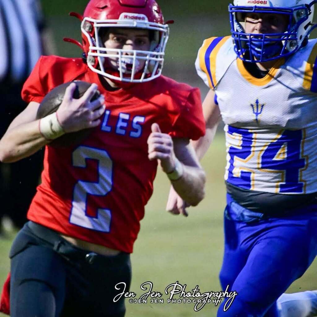 Two football players, one in red jersey number 2, the other in white and blue jersey number 24, run towards the camera.