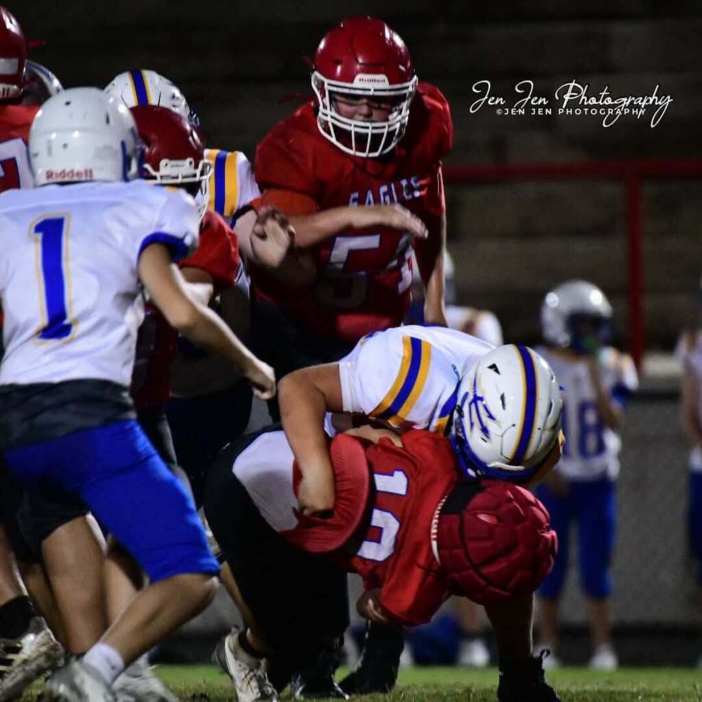 A group of young players in helmets and jerseys play football. One player lies on the ground.