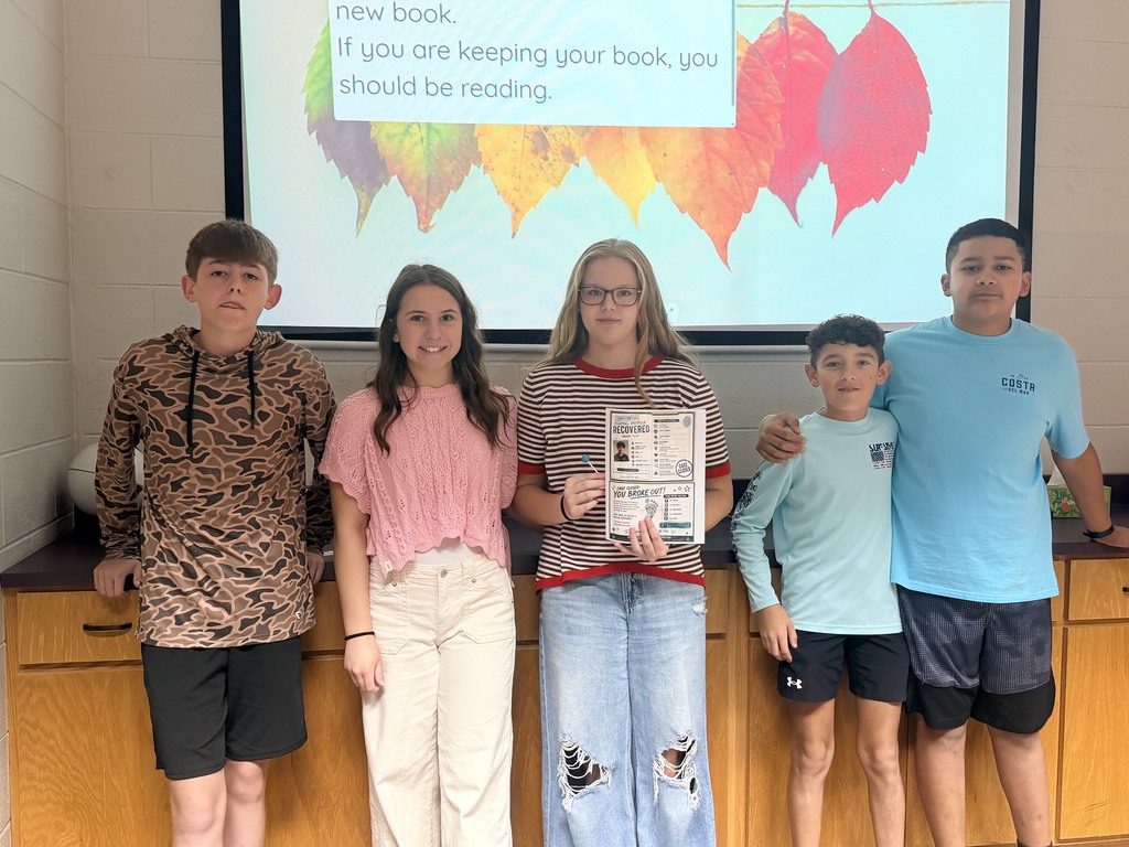 Five students stand before a screen displaying a book cover. The girl in the center holds a framed award.
