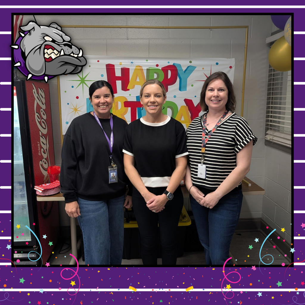 Three women in black and white tops and jeans stand in front of a birthday banner.