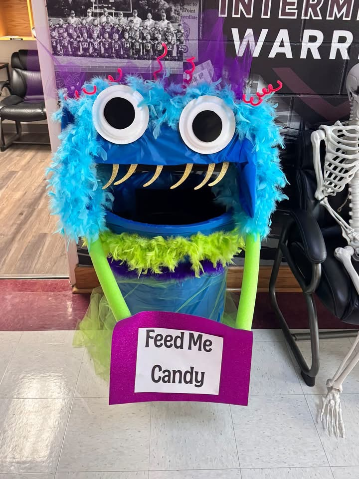 A blue and green monster with large eyes stands in front of a skeleton. The monster has a purple sign that reads, "Feed Me Candy."