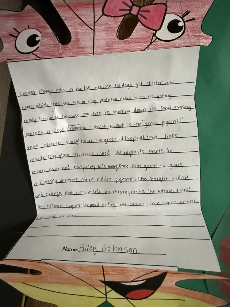 A paper in a pop-up book style with handwritten text, featuring a cartoon character with eyes, a bow, and a smile.