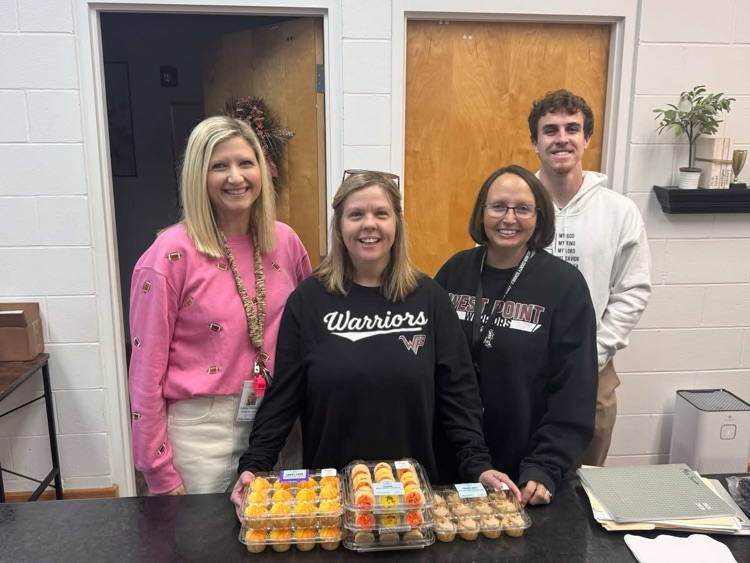 Four adults stand at a counter with trays of food. One woman wears a pink jacket.