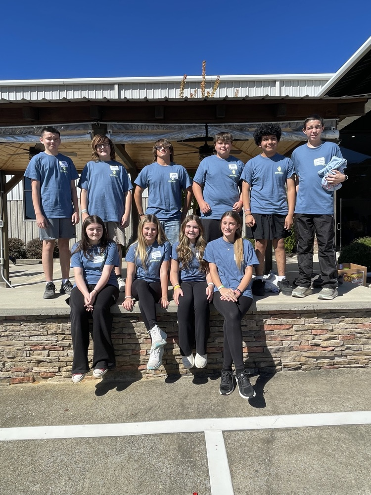 Group of young people in blue shirts and black pants posing for a photo outside.