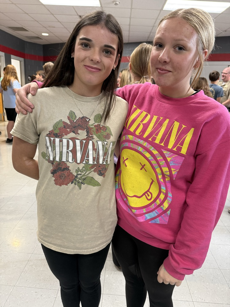 Two girls in sweatshirts smile for the camera. One wears a white shirt with a floral print.