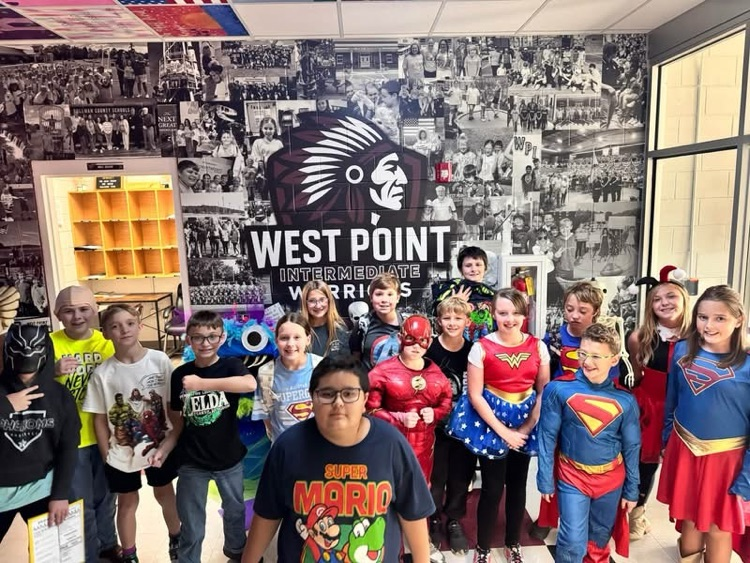 Students in costumes stand in a room with a large mural on the wall.