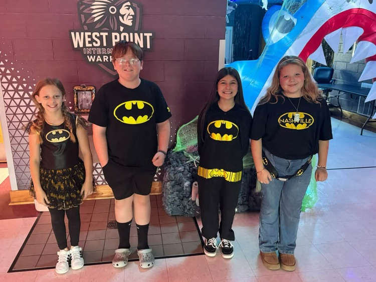 Four children in matching superhero costumes standing in front of a wall with a large shark decoration.