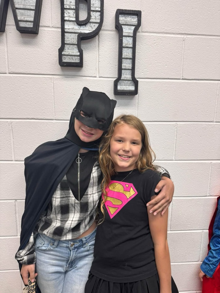 Two children pose for a photo. One wears a Batman costume, the other a Superman shirt.