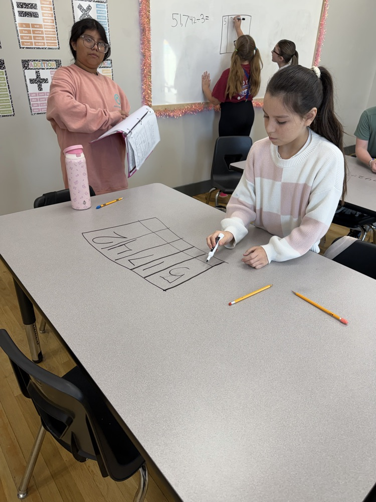 Students at a table draw a large grid on a dry-erase board with markers.