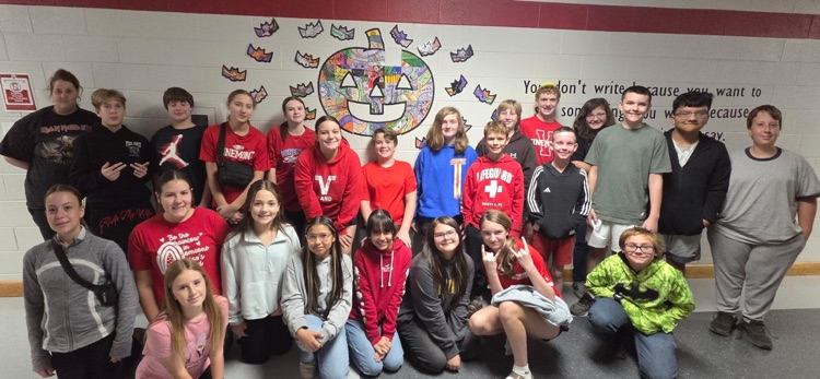 A group of students in various colors of shirts and jackets, posing together with a decorated wall behind them.
