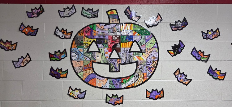 A wall with a large pumpkin face and smaller bat-shaped cutouts attached, creating a Halloween-themed display.
