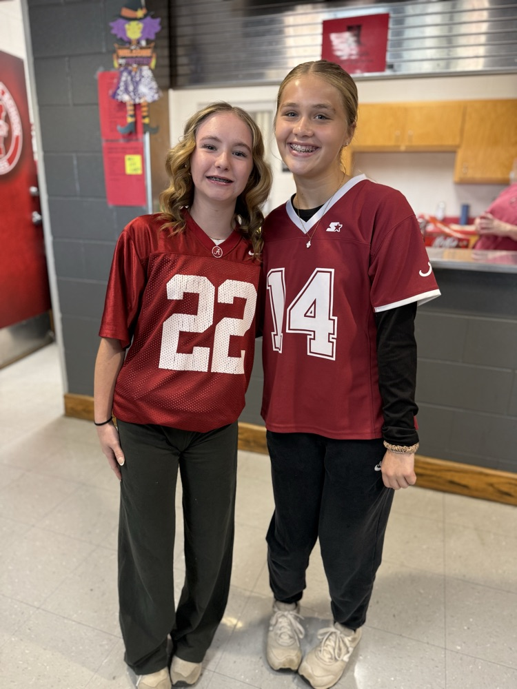 Two girls in maroon jerseys with numbers 22 and 14 stand together in a room with tiled floors.