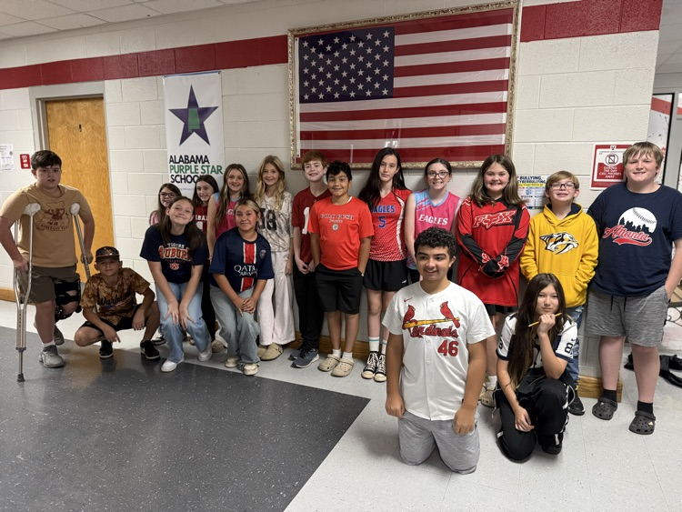 A group of students and adults pose for a picture in a room with a flag.