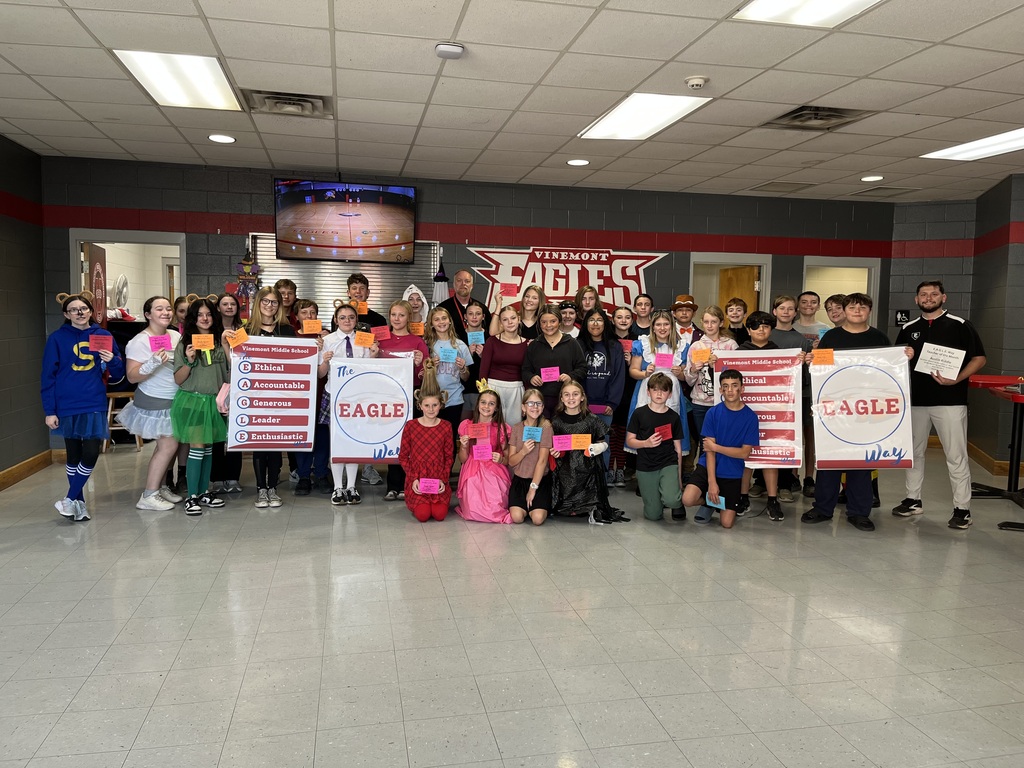 A group of people poses for a photo in a hallway, holding banners and wearing various outfits.