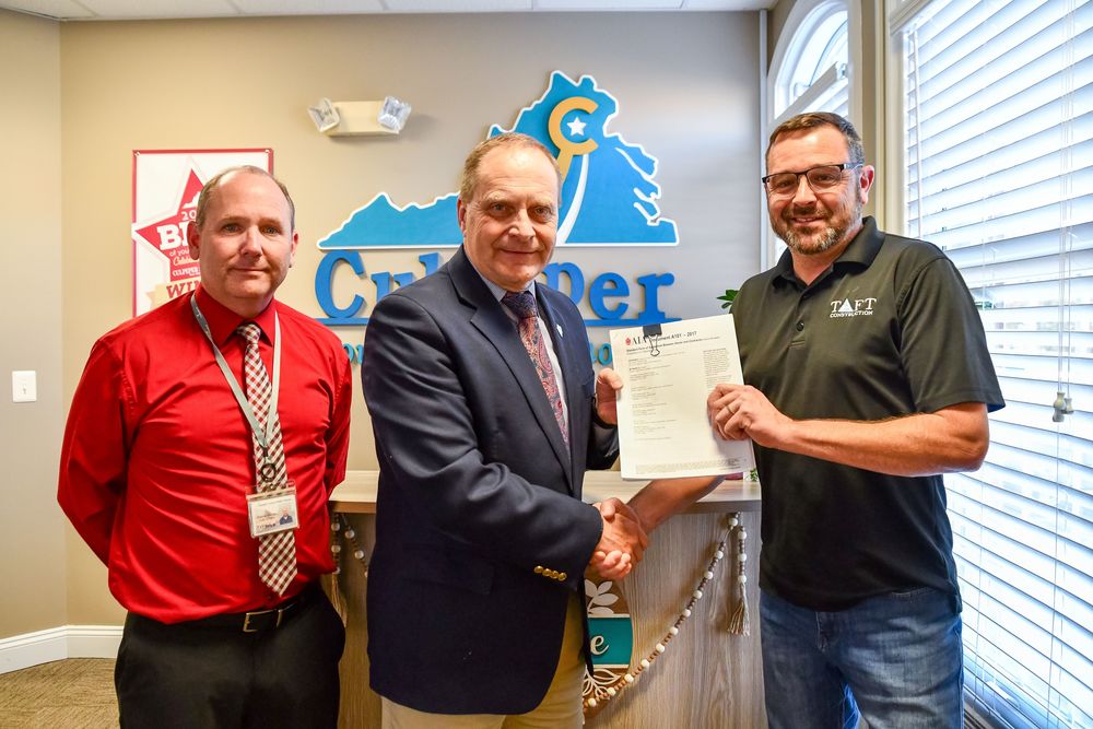 Superintendent Dr. Tony Brads shakes hands with a representative from Taft Construction while holding the signed construction contract for Mountain Run Elementary School. Another CCPS staff member stands beside them in the Culpeper County Public Schools administrative office.