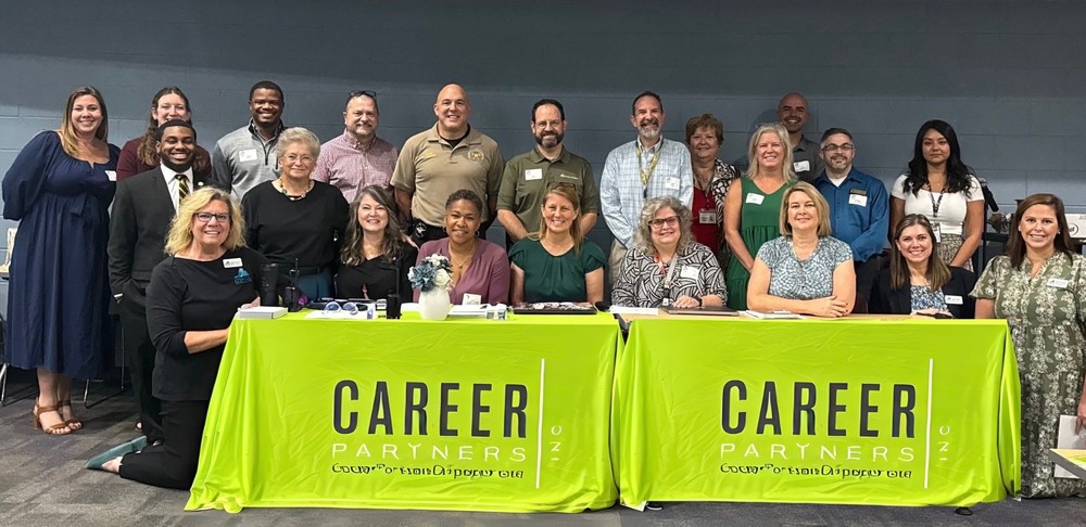 group of people standing behind 2 tables with bright green career partners table cloths on them.