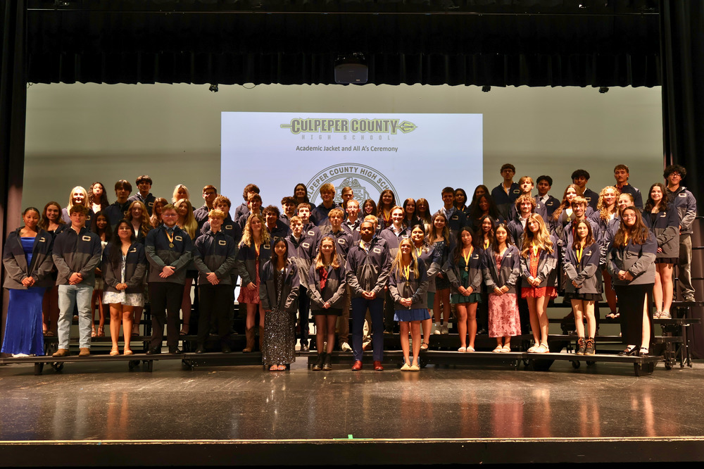 high school students standing on stage wearing academic jackets