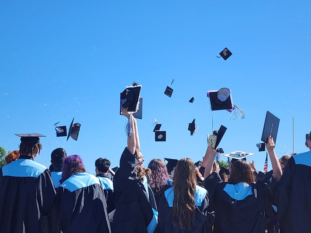 graduates throwing caps into the air under a beautiful blue sky