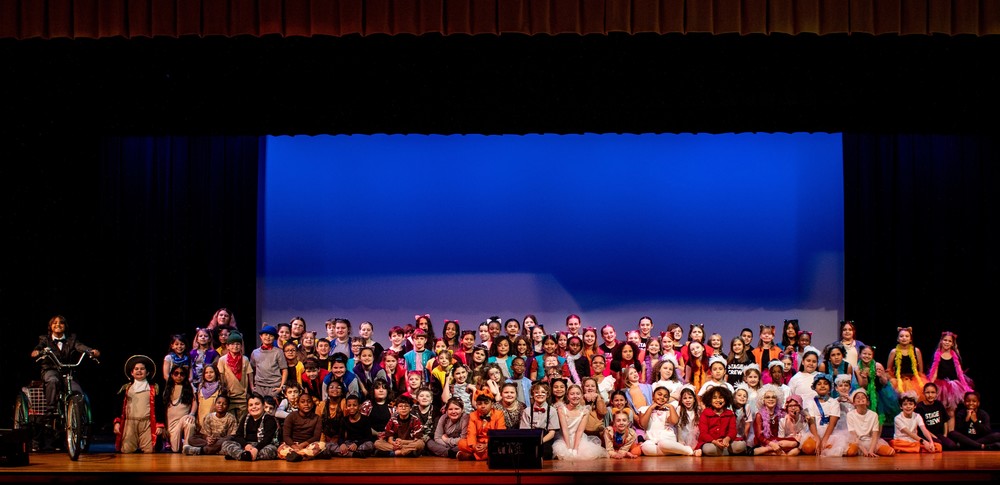 large group of elementary students in costumes on a school stage