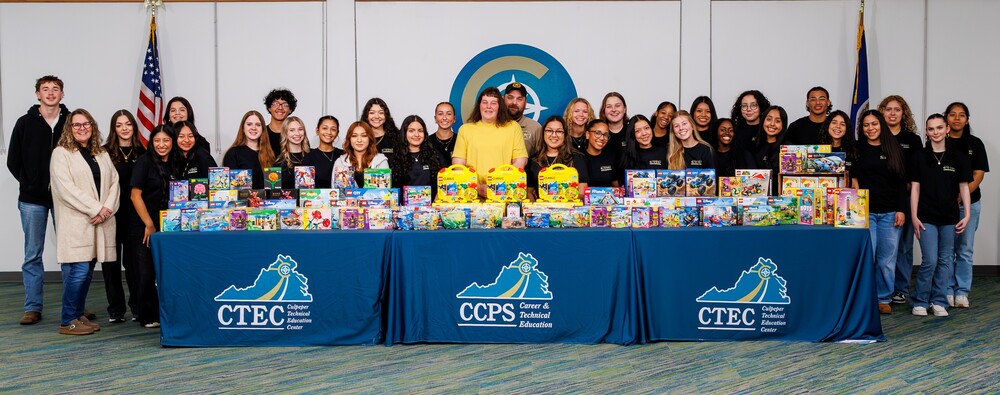 large group ofabout 40 students standing behind tables with CTEC and CCPS tablecloths on them with lego sets displayed on the tables