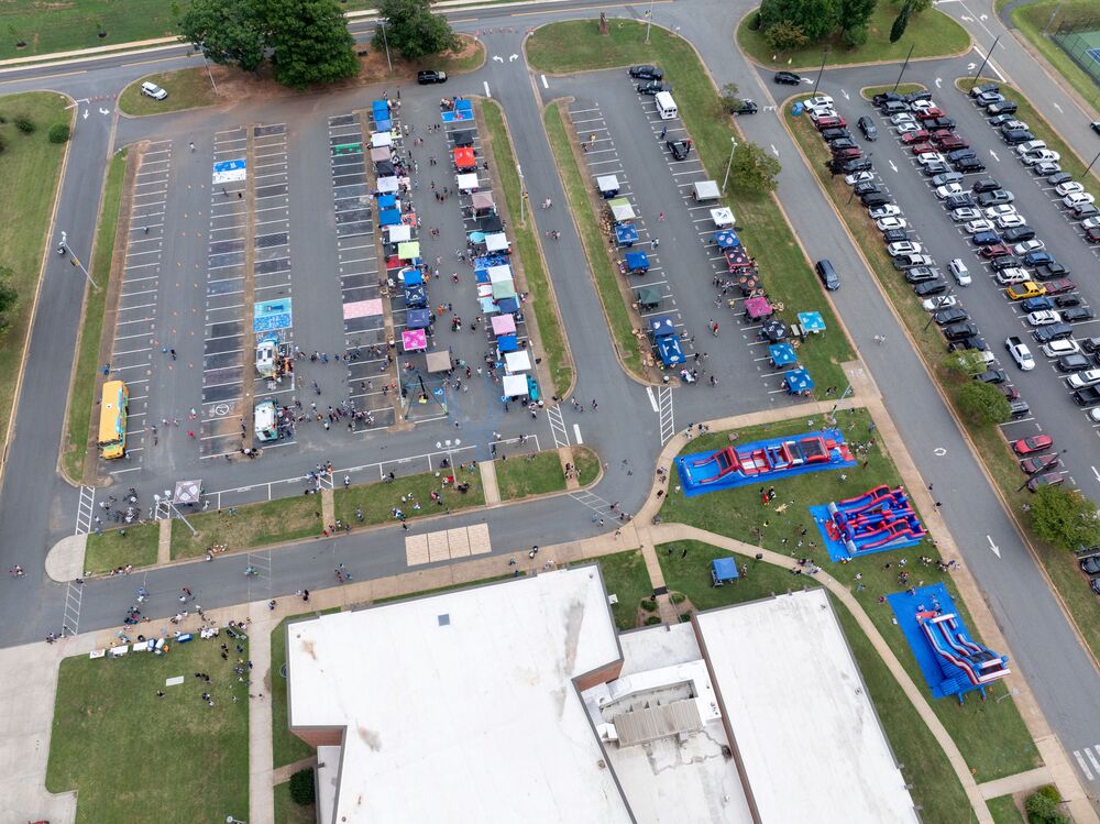 drone image of a parking lot filled with tents, there is a school bus and bicycles on the left and inflatable bounce houses on the right